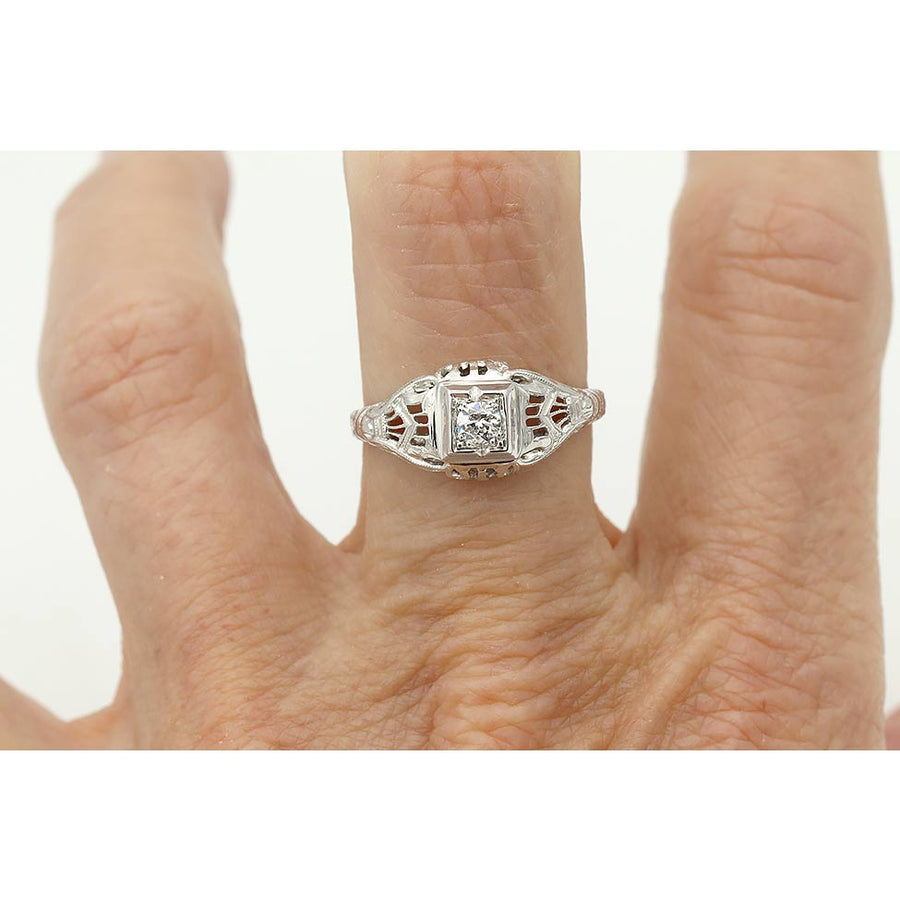 Art Deco old European cut diamond solitaire engagement ring in 18K white gold featuring a geometric square frame, open metalwork, and milgrain engraving on hand.